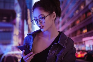Asian girl using a smartphone in the city at night. Portrait of an attractive young woman having fun outdoors, neon street lights on the background digital safety sexting safe sex contraceptives coronavirus
